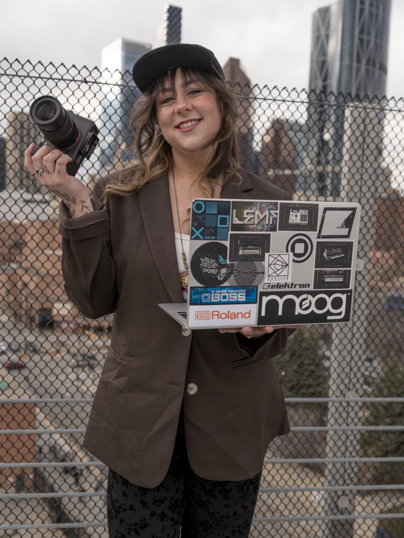 Ayrielle holding a camera and laptop on a Calgary rooftop.