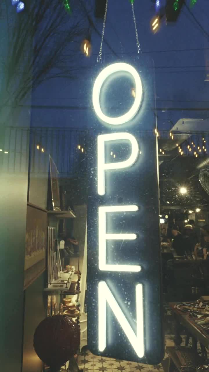 Glowing vertical OPEN sign in the Mercurius Curio storefront window with reflected lights and shop shelves behind it.